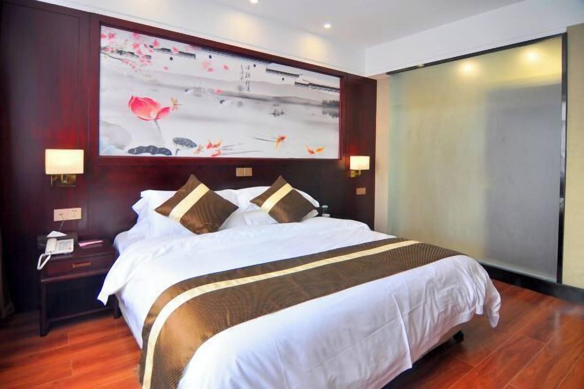 A hotel room with a large bed, dark wood paneling, a painting on the wall, and a sliding door.