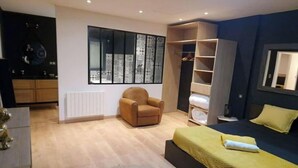 A modern bedroom with a large window, a wardrobe, a bed with a yellow bedspread, and a brown armchair.