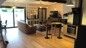 A modern living room with a sofa, coffee table, and a dining area with chairs. There is a kitchen with a microwave and oven.