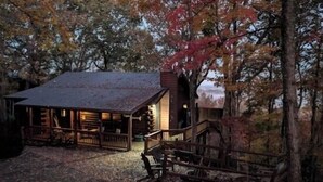 Une cabane rustique dotée d’un porche et d’une cheminée, entourée du feuillage automnal.