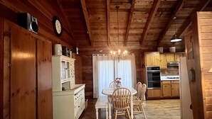 Un intérieur en bois comprenant une table à manger, des chaises, une cuisine équipée et une horloge murale.