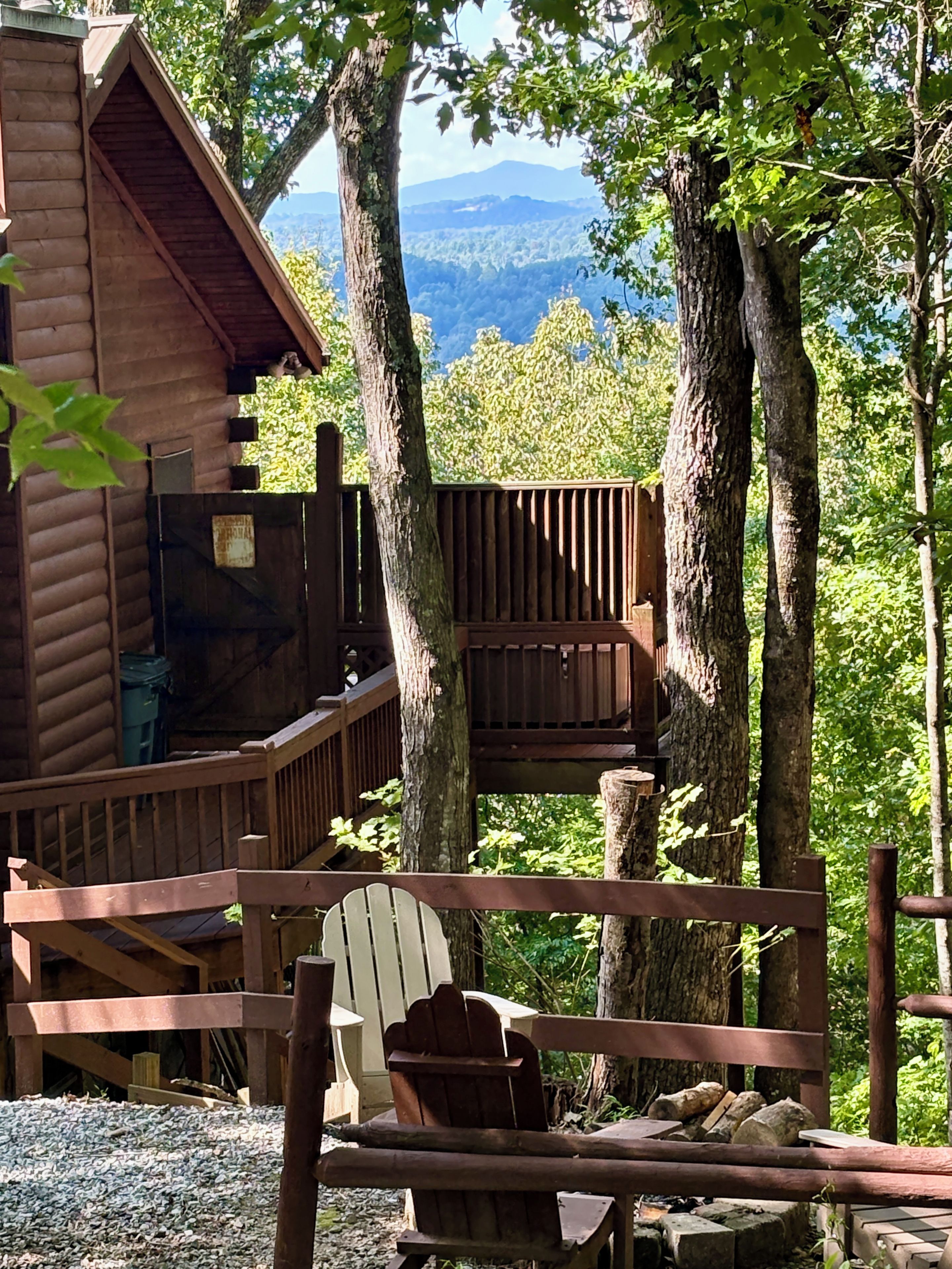 A cabin with a deck, surrounded by trees and a mountain view.