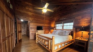 Une chambre dans un chalet en bois, avec un lit, un ventilateur de plafond, une télévision et une fenêtre.
