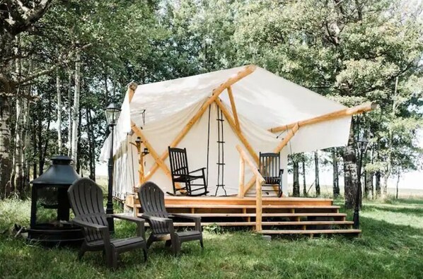 Relax in a serene forest setting, surrounded by trees and a cozy seating area with Adirondack chairs.