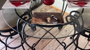 Une table en verre avec un cadre en métal, deux verres à vin, une bouteille de vin et une bougie rouge posés sur un plancher en bois.