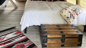 Een tentaccomodatie kamer met een bed, kussens, een houten kist en een vloerkleed.