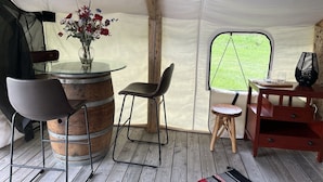 Een tent met een ronde glazen tafel, twee stoelen, een klein krukje en een houten bijzettafeltje met een bloevas.