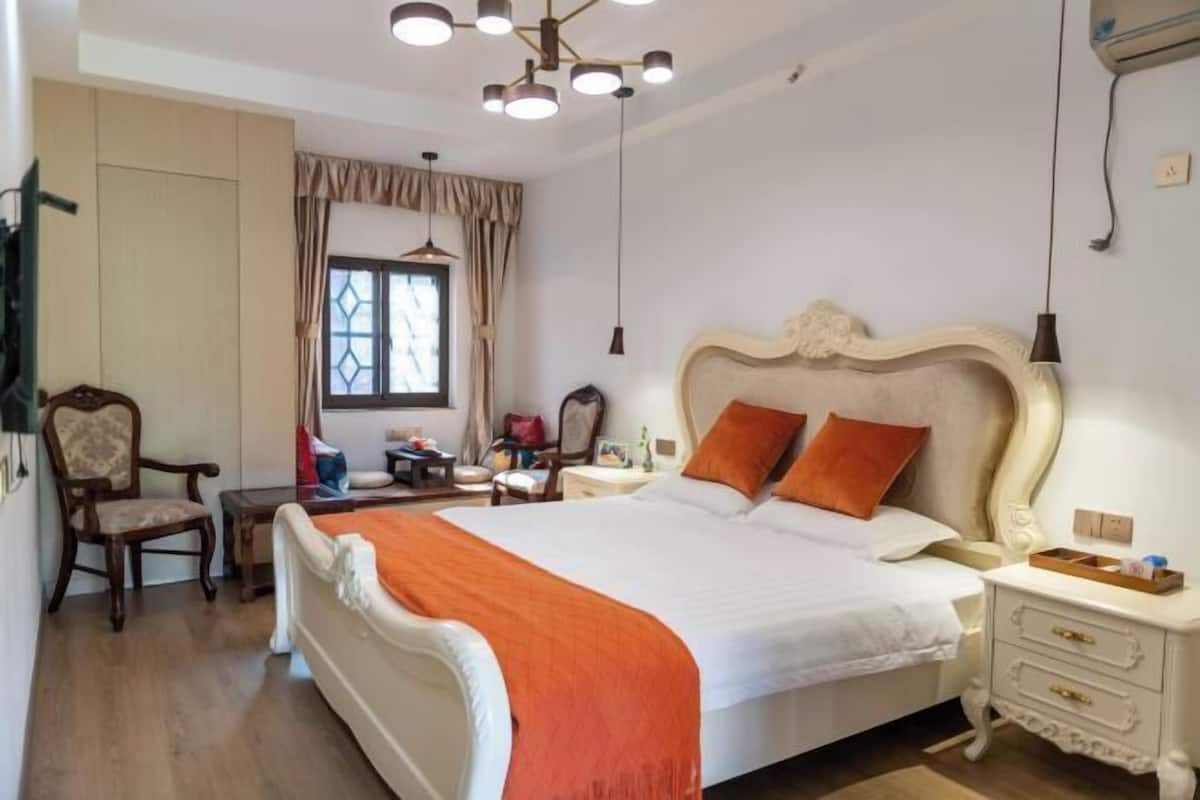 A bedroom with a large bed, a chair, a desk, and a window with curtains.