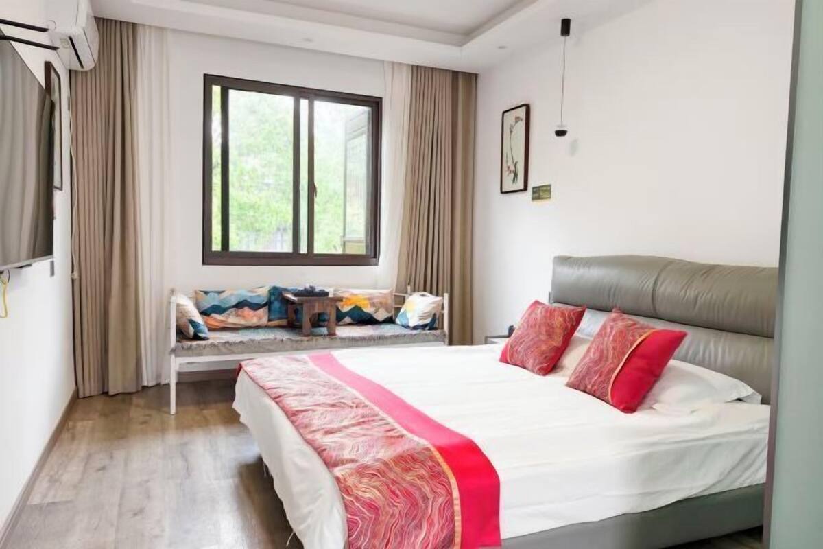 A bedroom with a bed, a window, curtains, and a wall-mounted picture.
