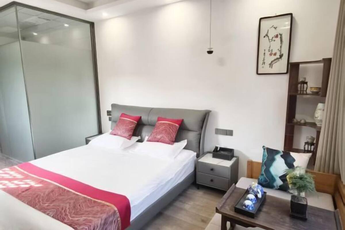 A modern bedroom with a bed, bedside tables, a nightstand, a small table with decorative items, and a wall-mounted shelf.