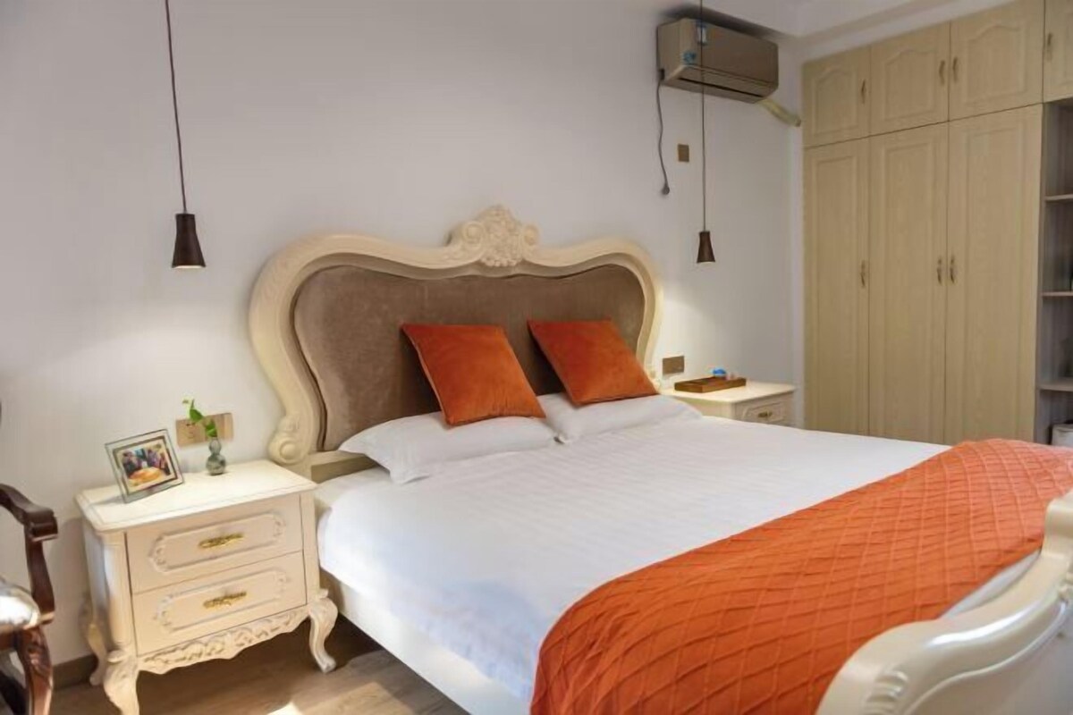 A bedroom with a bed, nightstand, dresser, wardrobe, and pendant lights.