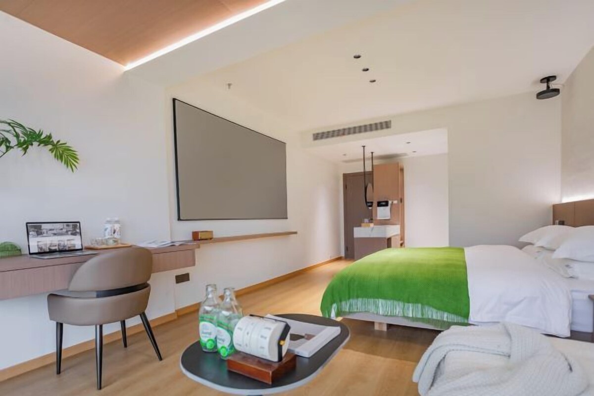A modern hotel room with a bed, desk, chair, and a large mirror.