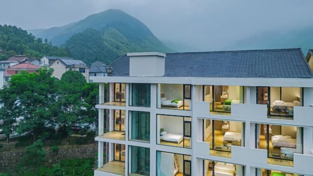 A modern hotel with multiple floors, large windows, and a view of a mountain. - Anji Shanya Minsu Guesthouse (Anji)