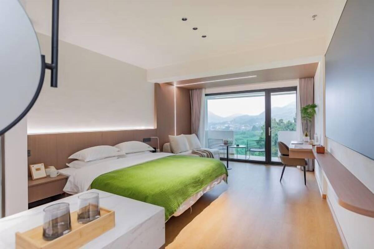 A modern hotel room with a large bed, a desk, a chair, and a view of the outdoors.