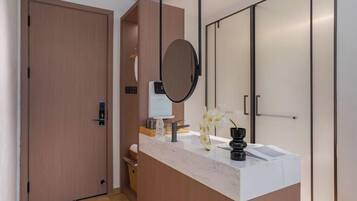 Une salle de bain moderne avec une porte en bois, un comptoir en marbre, un miroir rond et un petit lavabo.