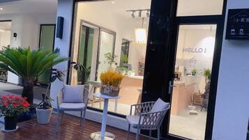 A hotel entrance with a glass door, a 'HELLO!' sign, and outdoor seating with chairs and a table.