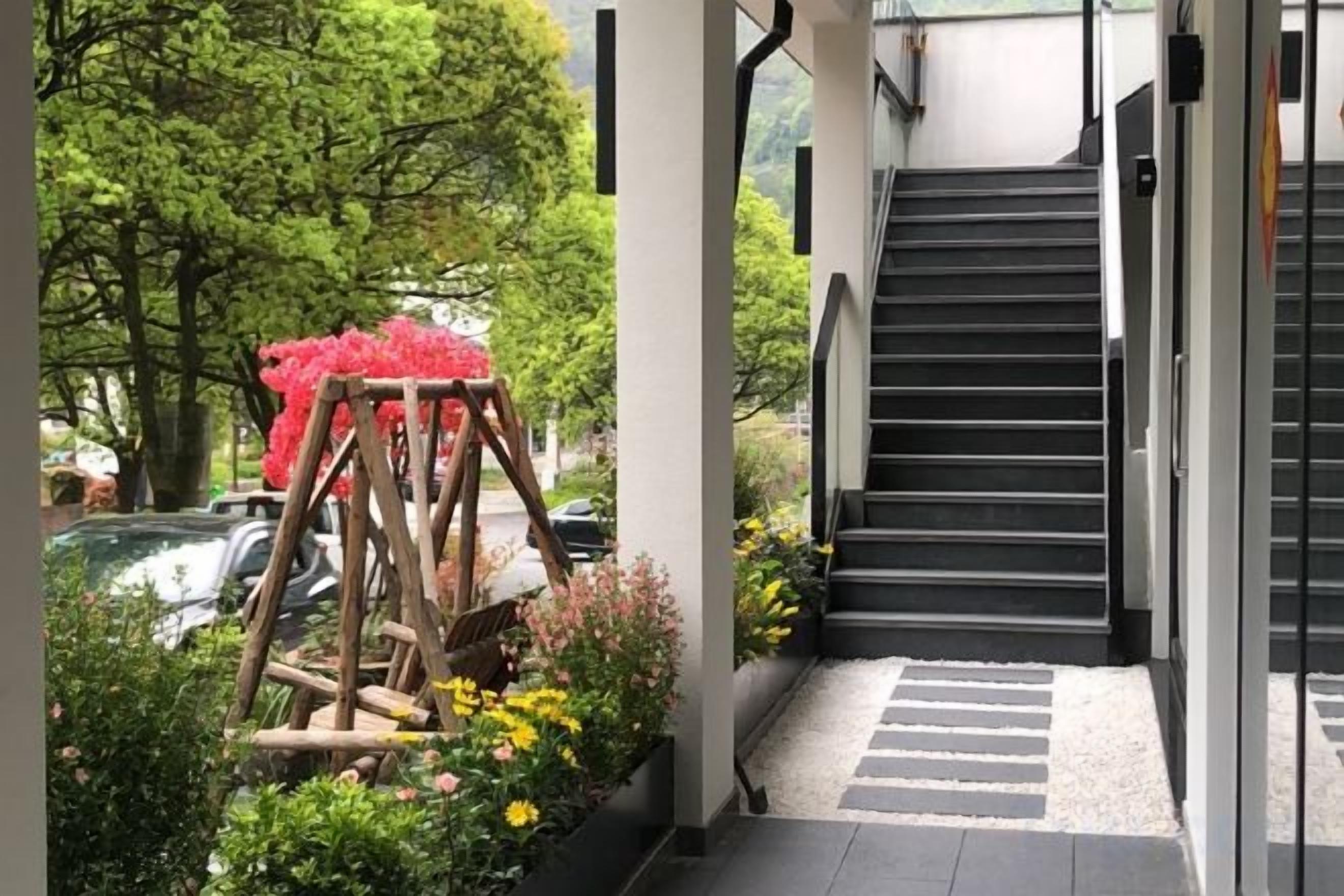 Unes escales condueixen a la porta d'un edifici, envoltades de vegetació i una estructura de fusta decorativa.