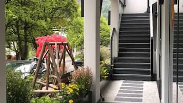 Unes escales condueixen a la porta d'un edifici, envoltades de vegetació i una estructura de fusta decorativa.