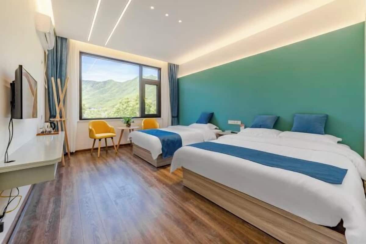 A hotel room with two beds, a desk, a chair, a TV, and a large window with a mountain view.