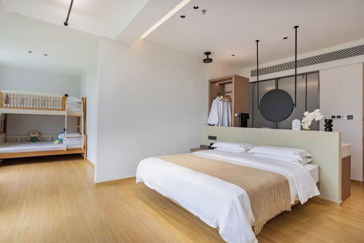 A modern bedroom with a large bed, a smaller bunk bed, a walk-in closet, and a round mirror.