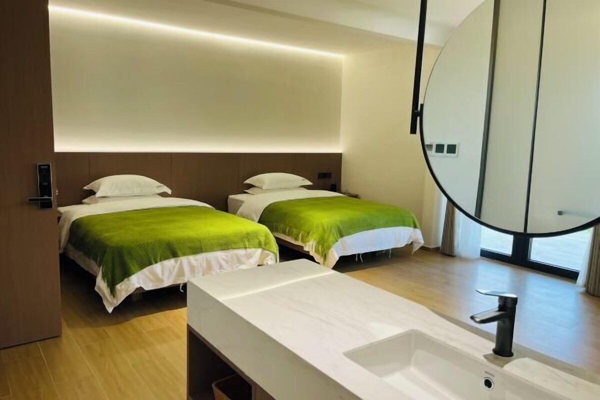 A modern hotel room with two beds, a large mirror, and a white sink.