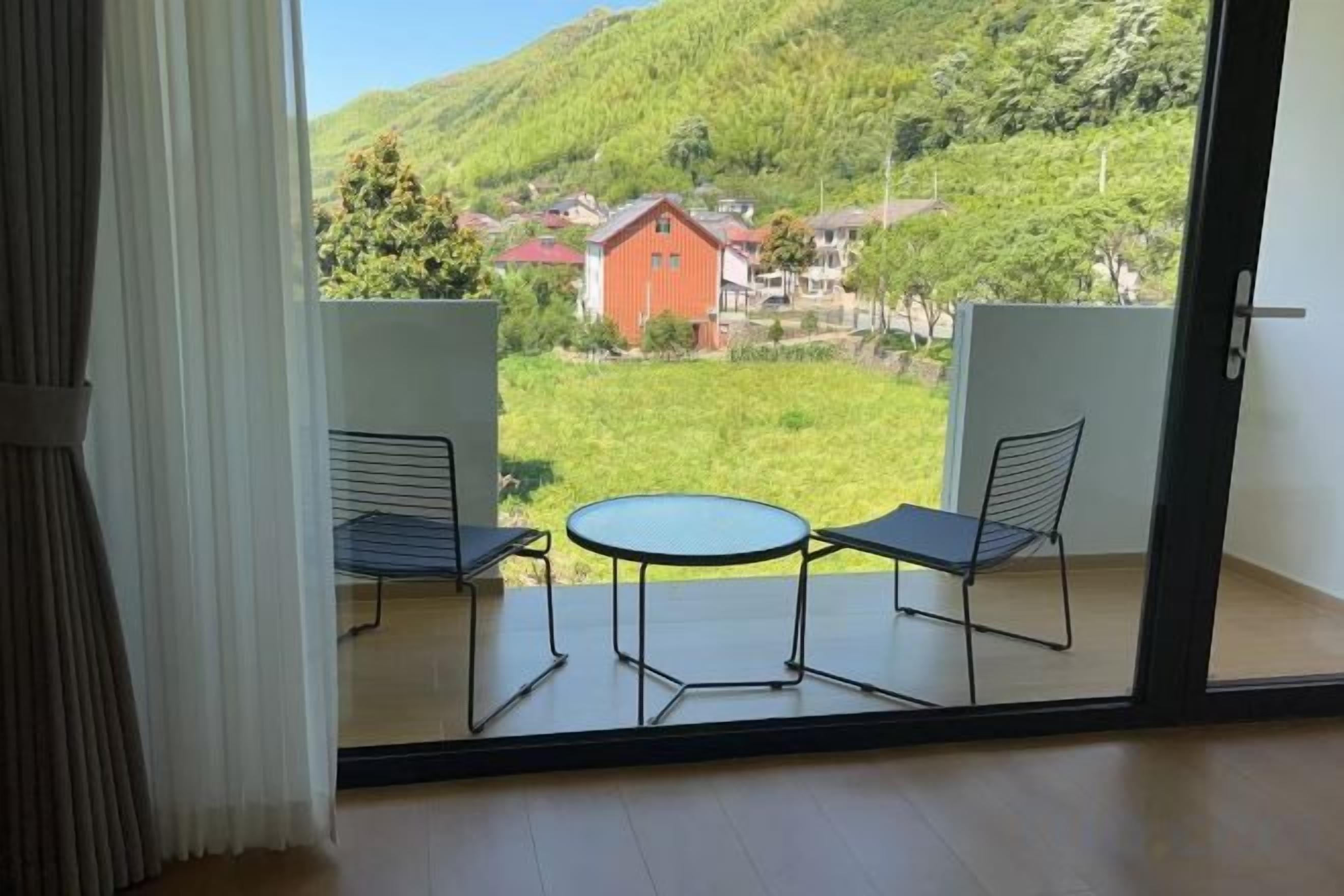 Varanda com mesa e duas cadeiras, com vista para uma paisagem verde com casas.