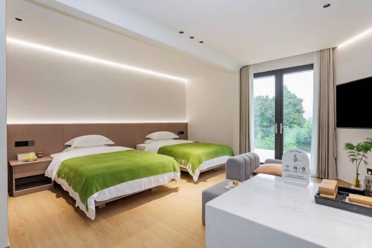 A hotel room with two beds, a desk, a TV, and a large window.