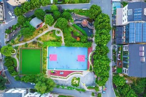 Vista aérea de un parque con cancha de baloncesto, rodeado de árboles y senderos.