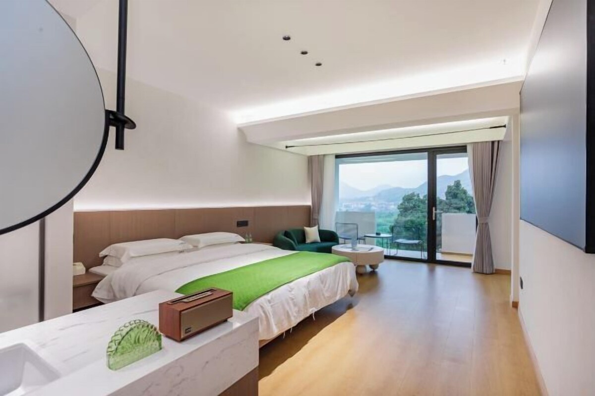A modern hotel room with a large bed, a desk, and a balcony with a view.