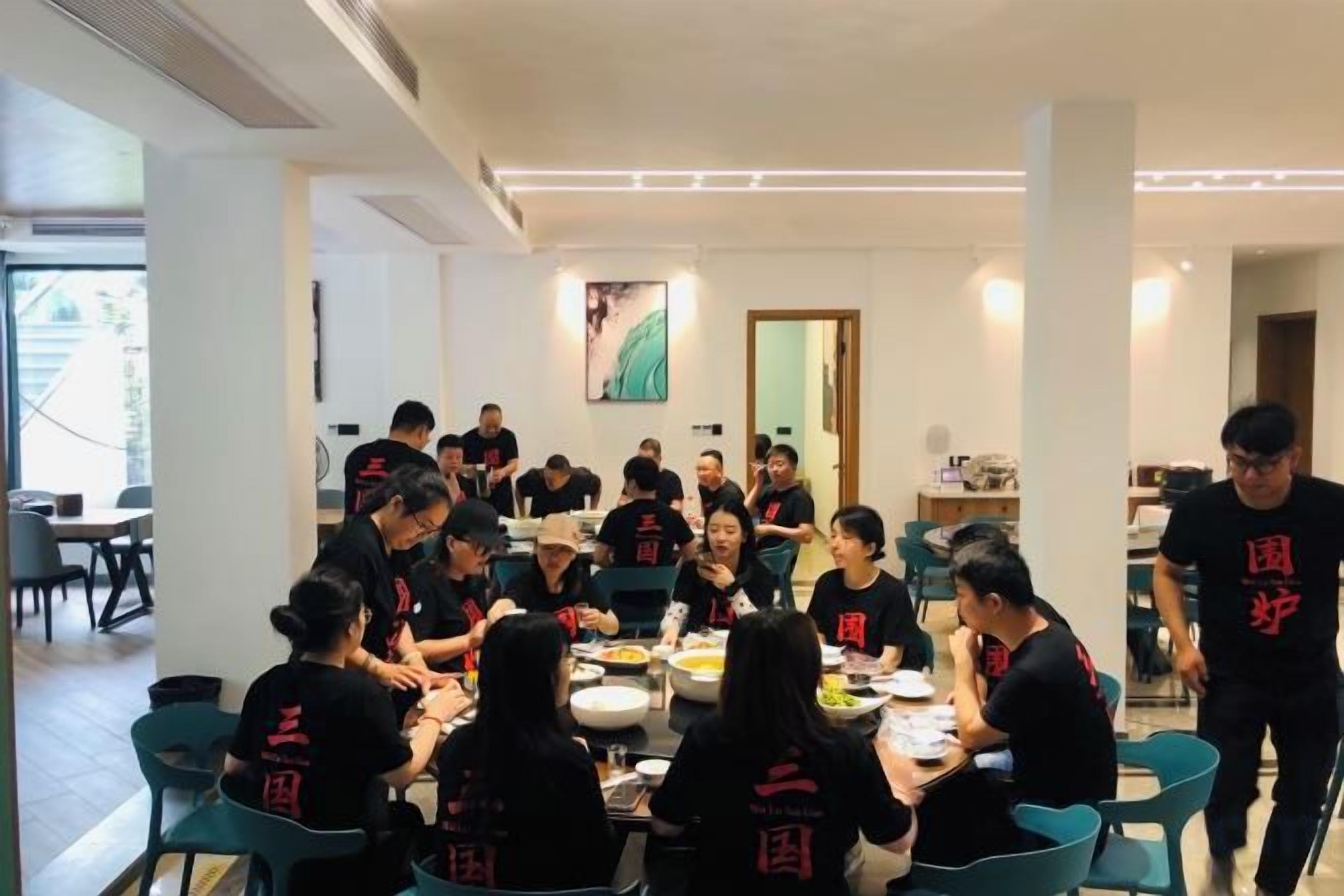 Grupo de pessoas sentado à mesa em espaço interno bem iluminado, com design moderno, destacando uma janela grande e uma porta ao fundo.