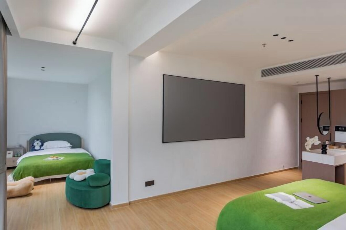 A modern hotel room with a large bed, a smaller bed, a green ottoman, a large mirror, and a flat-screen TV.