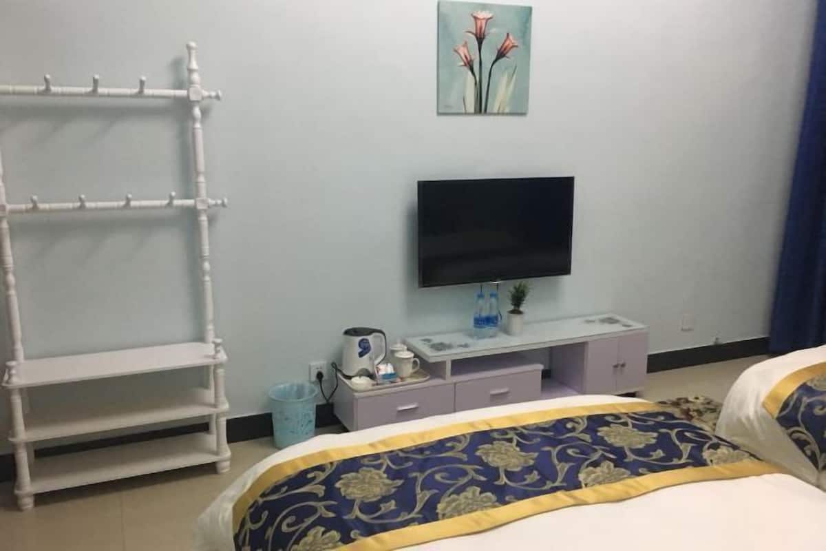 A hotel room with a bed, a TV, a small table with a kettle, and a shelf unit.