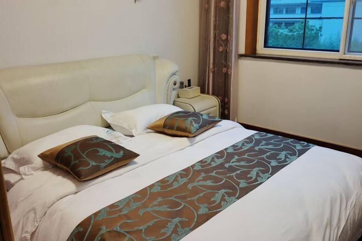 A hotel room with a bed, pillows, a bedside table, and a window.