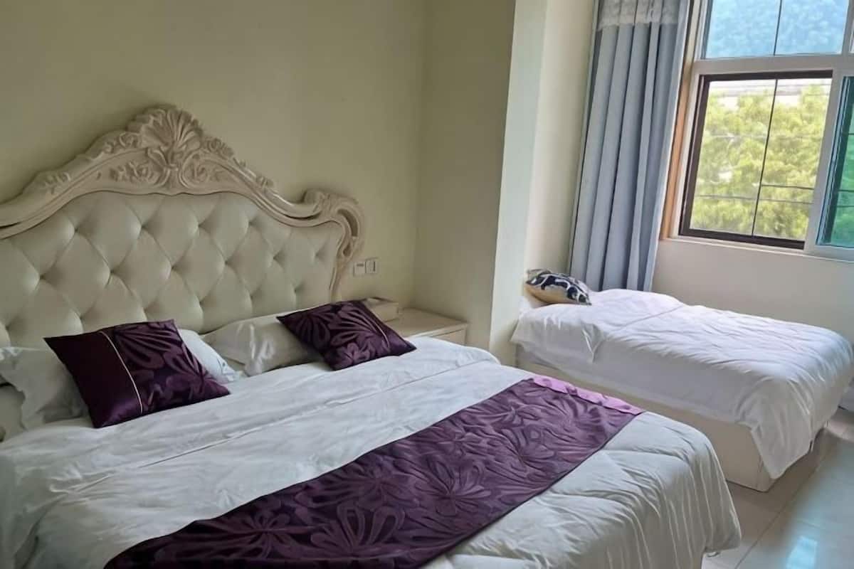 A bedroom with two beds, a large window, and a nightstand with a lamp.