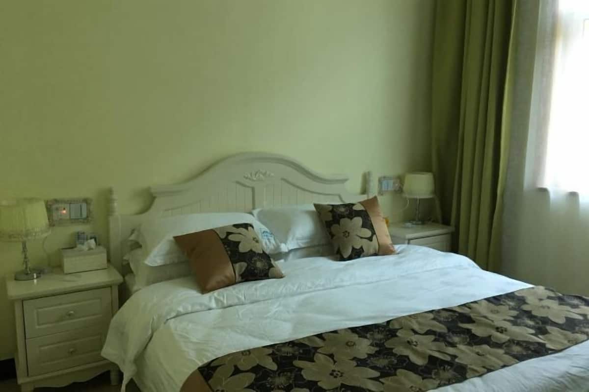 A bed with a floral bedspread, two pillows with a similar design, a nightstand with a lamp, and a bedside table with a lamp.