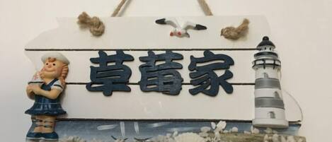 Een decoratief bord met een vuurtoren en een figuur, mogelijk een kok, met de tekst '草蕾家'.