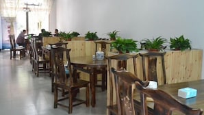 Un restaurante con mesas y sillas de madera, plantas en macetas y una persona al fondo.