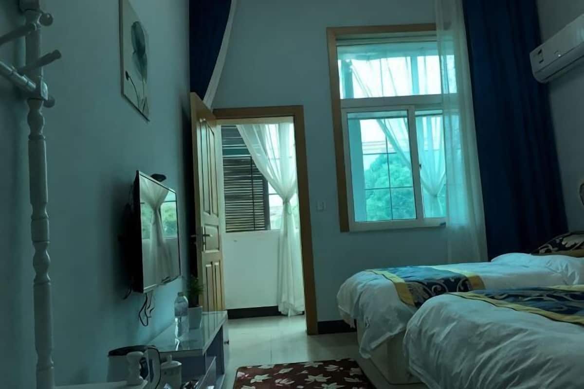 A bedroom with a bed, a dresser, a TV, a window with curtains, and a door leading to another room.