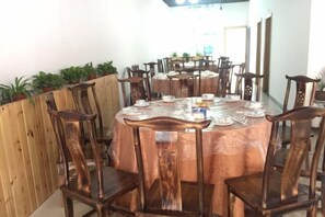 A dining area with round tables, wooden chairs, and potted plants. - Aimo Inn (Deqing)