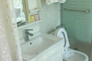 Un bagno con un lavandino bianco, un water, uno specchio e uno scaffale con articoli da toilette.