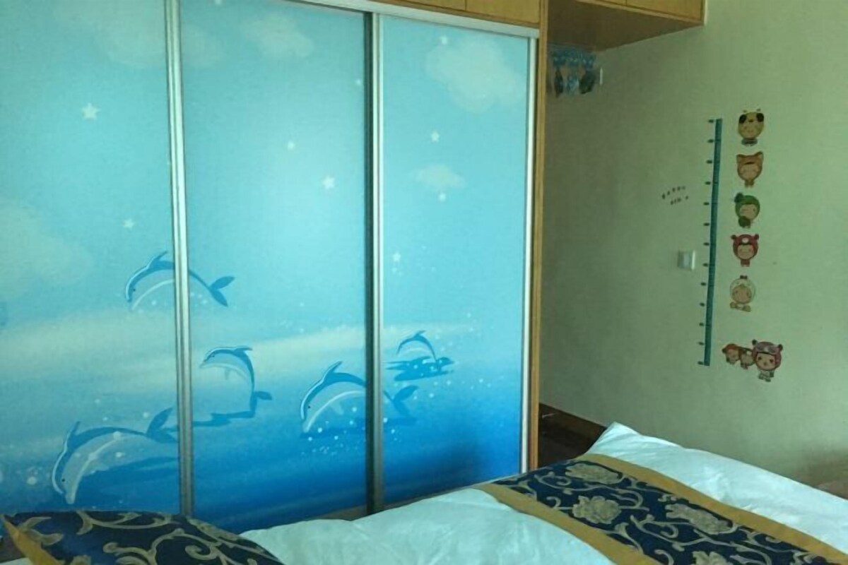 A bedroom with a bed, a wardrobe with dolphin decals, a growth chart on the wall, and a window with a view.