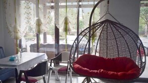 Un comedor con mesa y sillas, un sillón colgante con cojín rojo, y vistas al exterior a través de grandes ventanales.