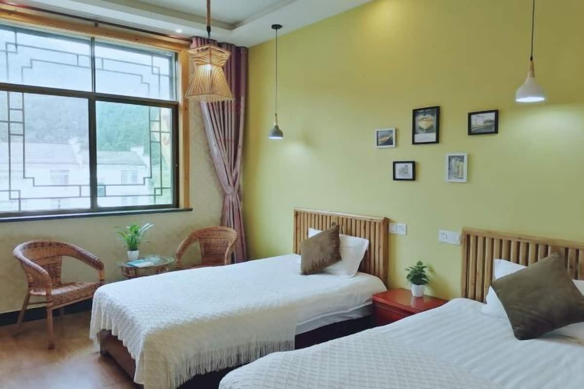Una habitación con dos camas, sillas de mimbre, una mesita con una planta y una ventana con cortinas.