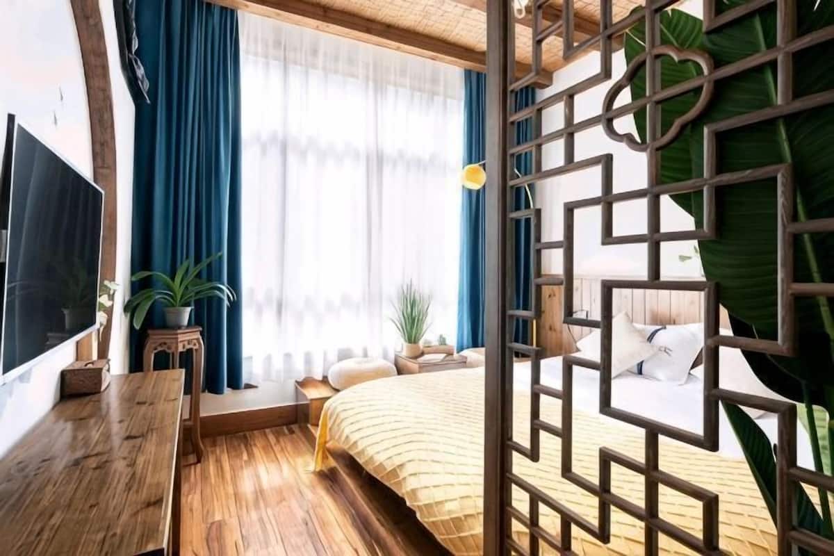 Un dormitorio con cama, televisor, escritorio y ventana con cortinas.