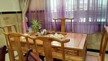 Una mesa de comedor de madera con sillas, una planta en maceta y un ventanal con cortinas moradas.