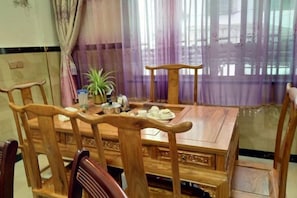 A wooden dining table with chairs, a potted plant, and a window with purple curtains.