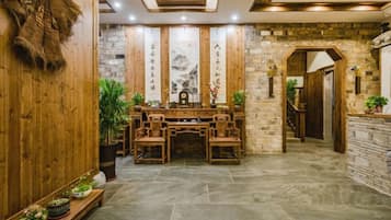 Un interior tradicional de madera con una mesa central y sillas, paredes de piedra y una escalera que lleva a un nivel superior.