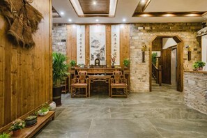 A traditional wooden interior with a central table and chairs, stone walls, and a staircase leading to an upper level.