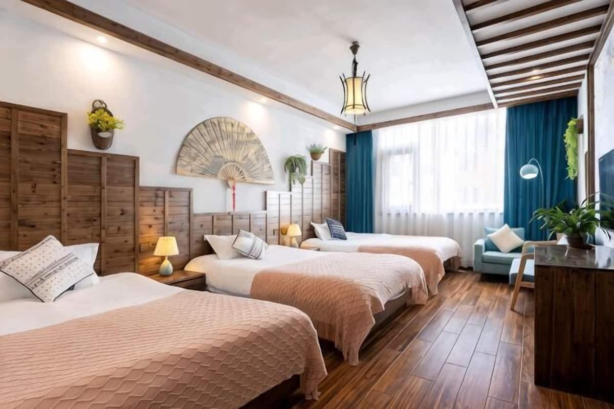 Habitación de hotel con tres camas, piso de madera, un escritorio y un ventilador.