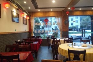A restaurant interior with tables and chairs, a brick wall, and a view through the window. - Wenjunge Jingju (Wuyuan)